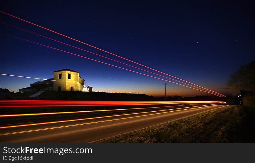 Traffic headlights and taillights on rural road past illuminated house at night. Traffic headlights and taillights on rural road past illuminated house at night.