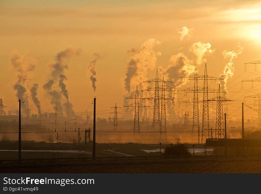 Industrial smokestacks with plumes of steam or pollution with electrical stanchions at sunset. Industrial smokestacks with plumes of steam or pollution with electrical stanchions at sunset.