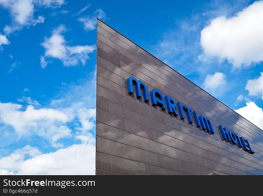 Blue Maritim Hotel signage on building exterior against blue sky with clouds. Blue Maritim Hotel signage on building exterior against blue sky with clouds.