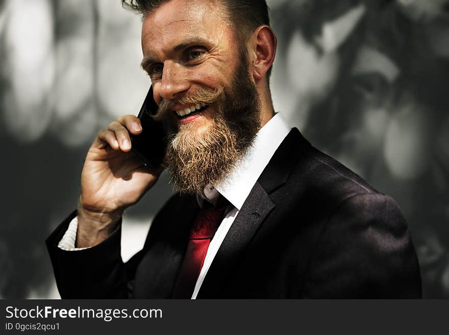 Portrait of smiling smartly dressed businessman listening (conversing) on mobile phone, blurred background. Portrait of smiling smartly dressed businessman listening (conversing) on mobile phone, blurred background.