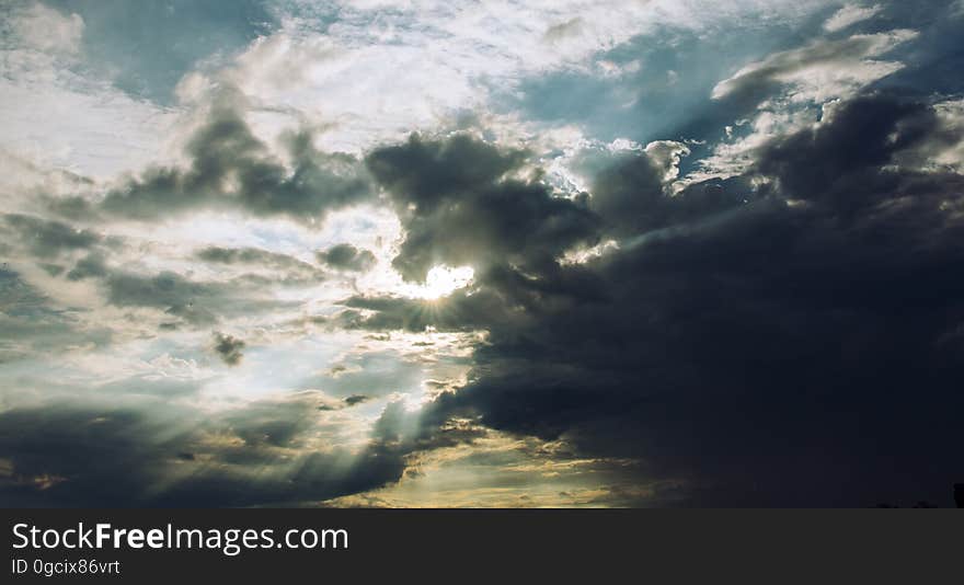 Sun with rays streaming through light and darkened storm clouds in the sky. Sun with rays streaming through light and darkened storm clouds in the sky.