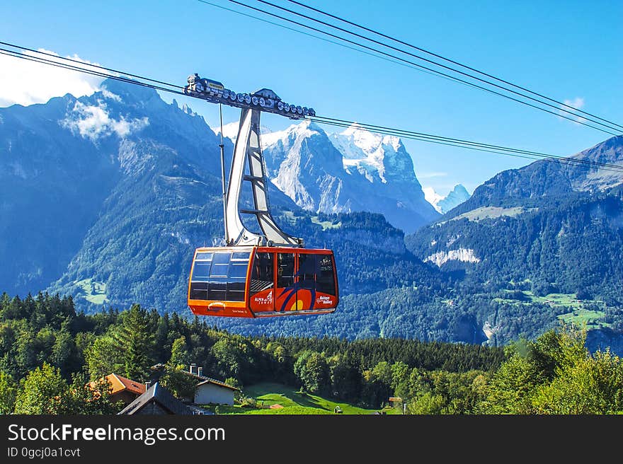 Red cable car traveling over mainly forested countryside into the snow covered mountains carrying skiers and or climbers, mountain background with blue sky. Red cable car traveling over mainly forested countryside into the snow covered mountains carrying skiers and or climbers, mountain background with blue sky.