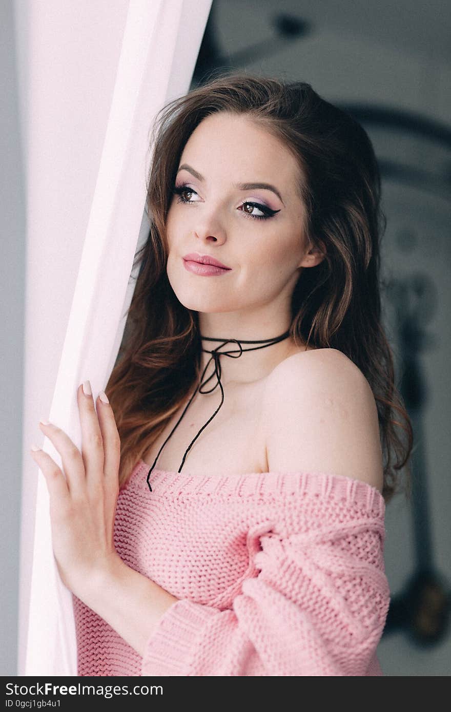 Pretty woman wearing pink woven dress and necklace looking pensively around a curtain perhaps expecting a guest or lover. Pretty woman wearing pink woven dress and necklace looking pensively around a curtain perhaps expecting a guest or lover.