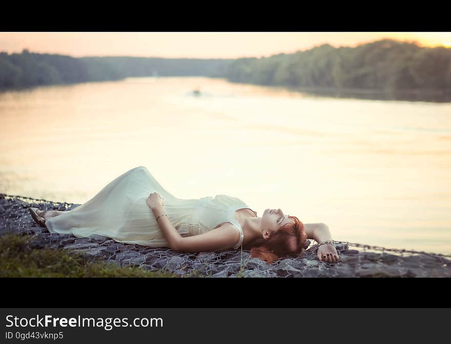 A woman in long dress lying on a shore of a river or a lake. A woman in long dress lying on a shore of a river or a lake.