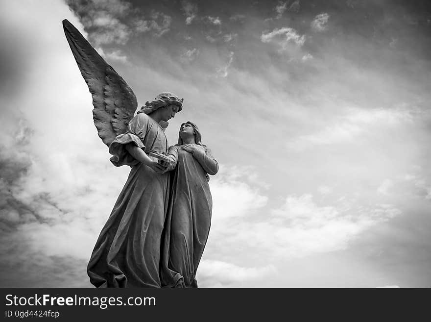 A black and white statue of a winged angel against the sky. A black and white statue of a winged angel against the sky.