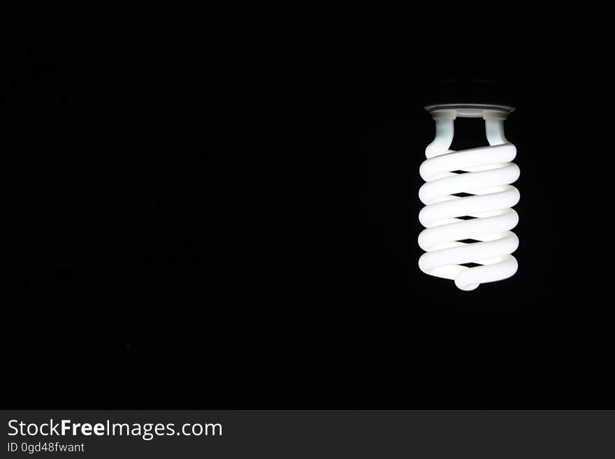 A spiral-shaped light bulb on black background. A spiral-shaped light bulb on black background.