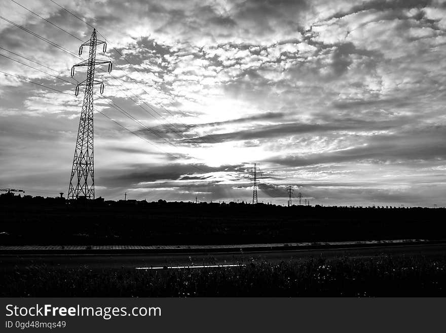 Electricity pylons stretching into the distance in a dark landscape at dawn fluffy gray clouds. Electricity pylons stretching into the distance in a dark landscape at dawn fluffy gray clouds.