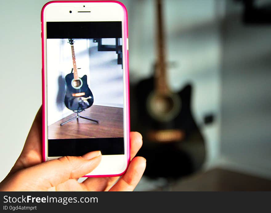 A person taking a photo of a guitar with a mobile phone. A person taking a photo of a guitar with a mobile phone.