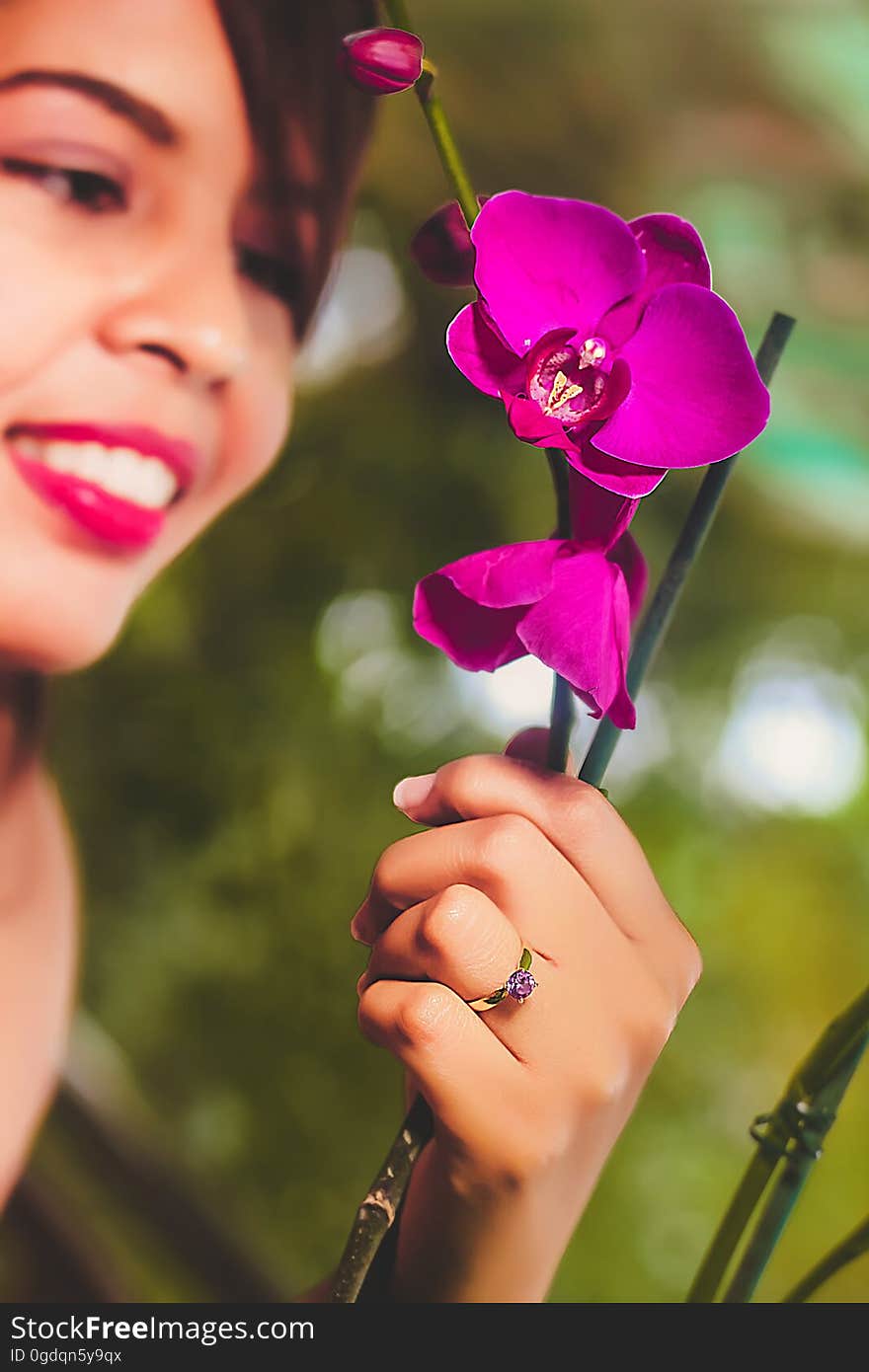 Smiling woman viewing her purple orchid flowers with selective focus on her ring and on the blooms. Smiling woman viewing her purple orchid flowers with selective focus on her ring and on the blooms.