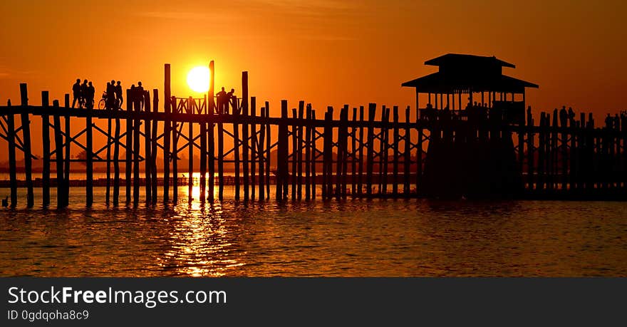 People walk on a pier at sunset.