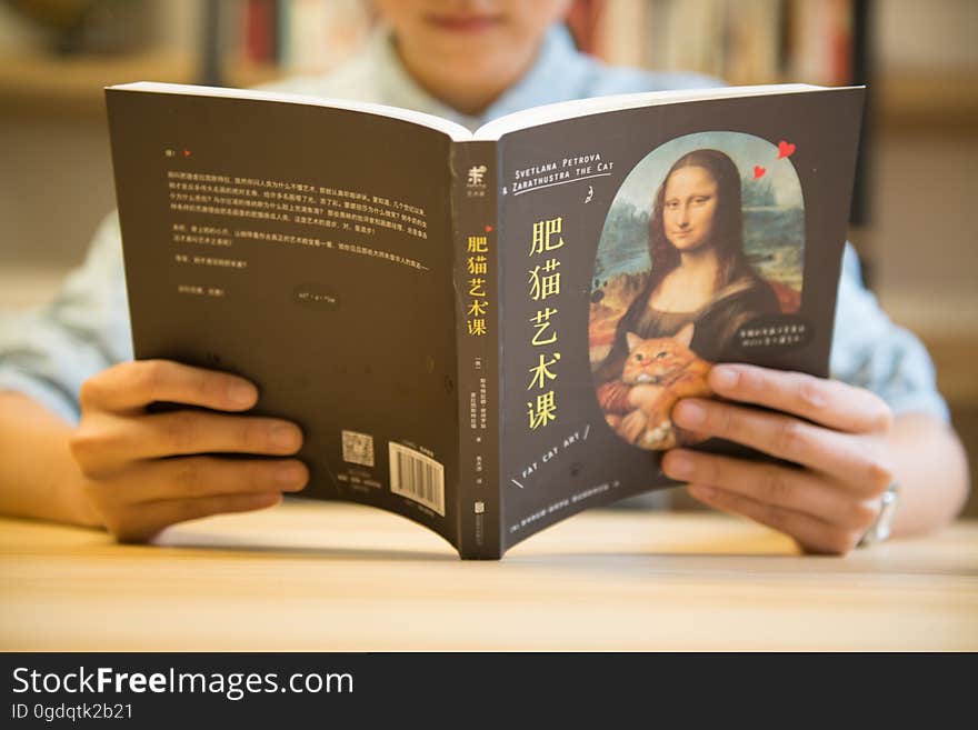 Closeup of the back of an open Japanese book held in the hands of an anonymous reader, with shallow depth of field focusing on the book and reader's hands. Closeup of the back of an open Japanese book held in the hands of an anonymous reader, with shallow depth of field focusing on the book and reader's hands.