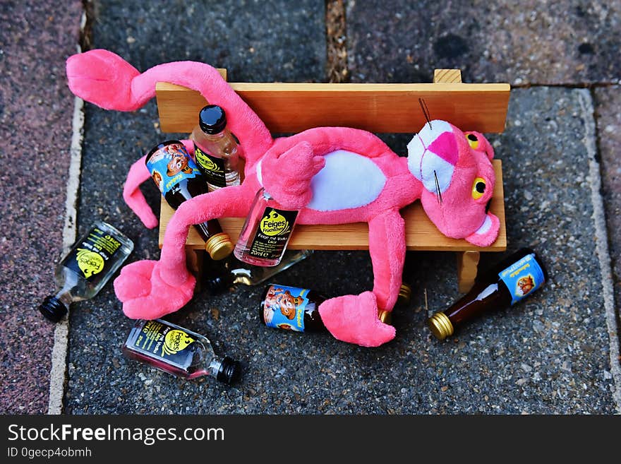 A pink panther on a wooden bench with empty bottles.