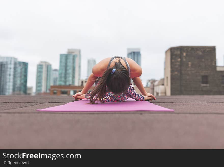 Woman performing yoga on building roof with city skyline in background.