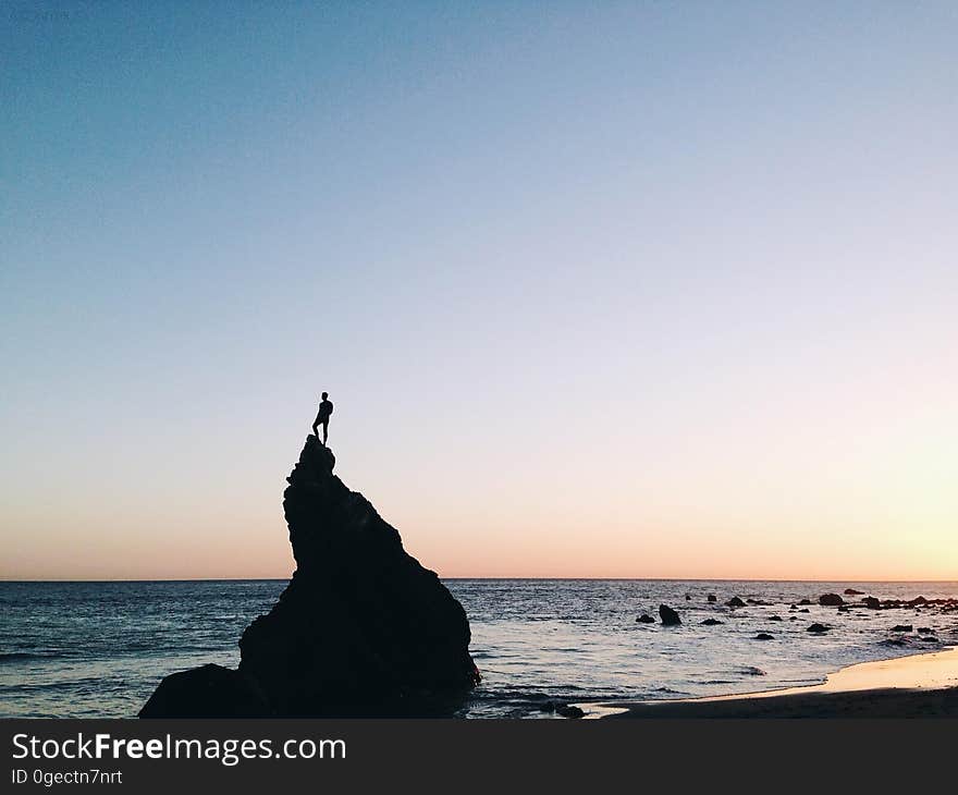 Silhouette of Person Standing on Rock on Beach Shore during Yellow Sunset