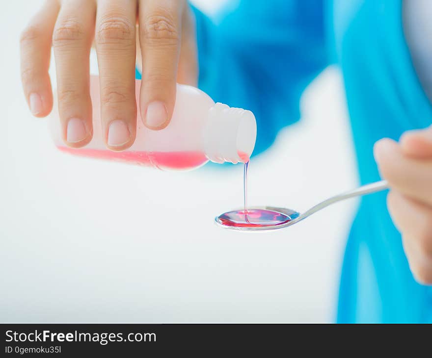 Healthcare, people and medicine concept - woman pouring medication or antipyretic syrup from bottle to spoon