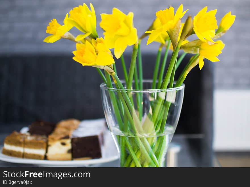 A vase of daffodils resting on a table with a desert tray behind it.