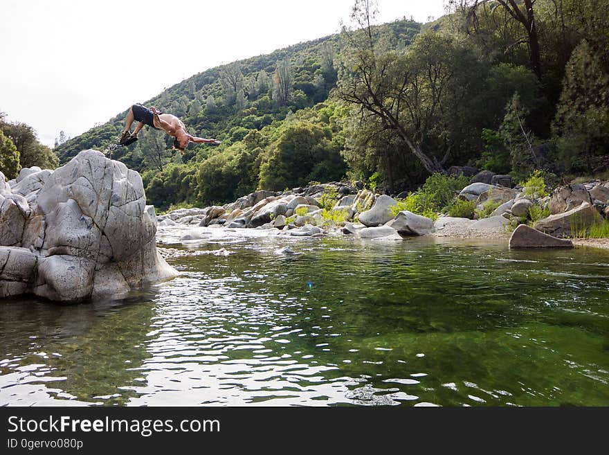 Man in Black Shorts Back Flipping Into River during Daytime