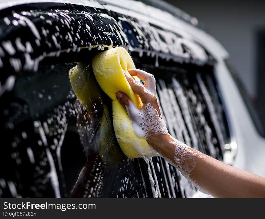 Woman hand with yellow sponge washing car