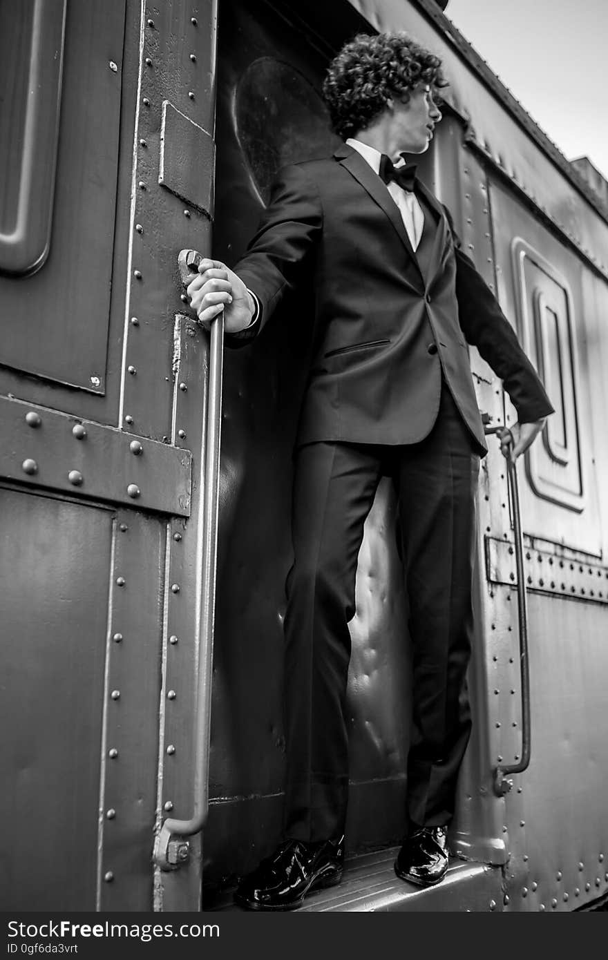 A man wearing a suit standing on the doorway of a train. A man wearing a suit standing on the doorway of a train.