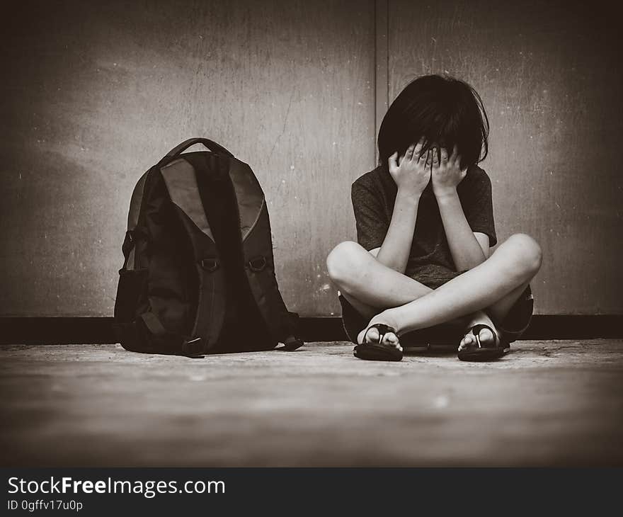 Sad Kid Sitting On The Floor With School Bag Waiting For Parent.