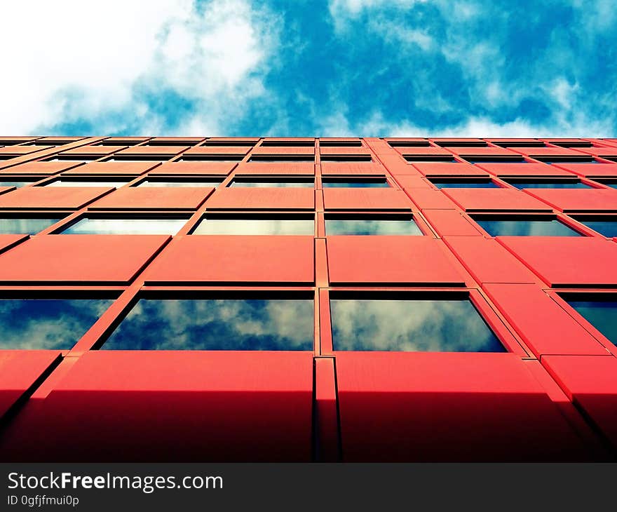 Architectural design with concrete, steel and glass and red panels (thermal cladding perhaps) livened by blue sky and white clouds reflected in the glass windows. Architectural design with concrete, steel and glass and red panels (thermal cladding perhaps) livened by blue sky and white clouds reflected in the glass windows.