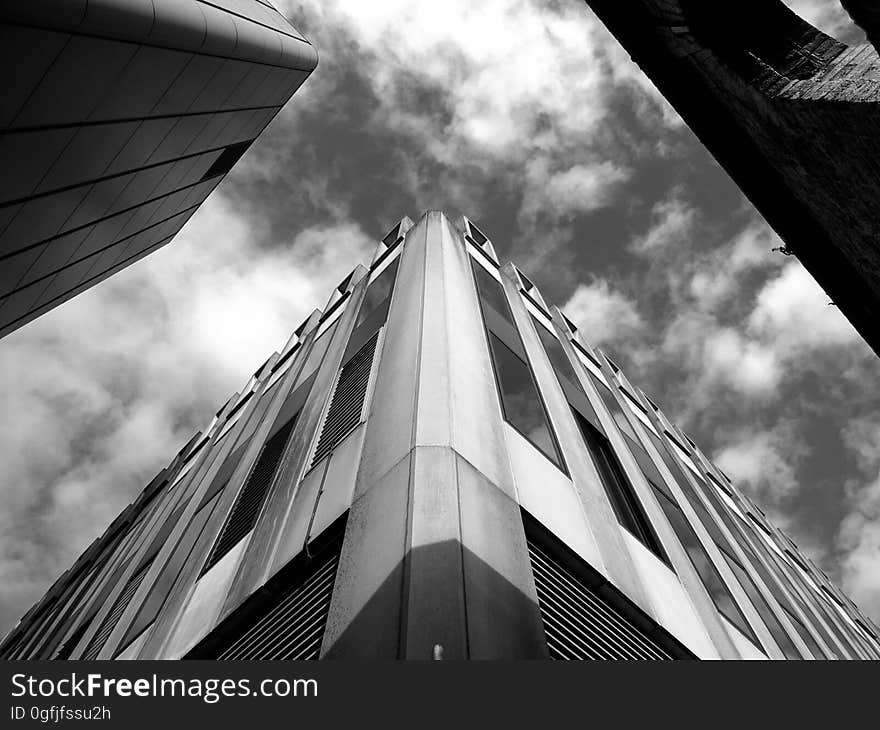 Building in futuristic architectural style constructed of glass, steel and concrete showing two adjacent sides of the building with the sharp corner flattened, background of sky and clouds. Building in futuristic architectural style constructed of glass, steel and concrete showing two adjacent sides of the building with the sharp corner flattened, background of sky and clouds.