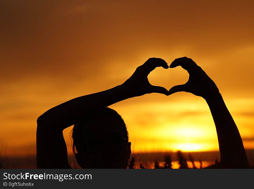 Silhouette Woman Hand Holding Heart Shape Against Orange Sky