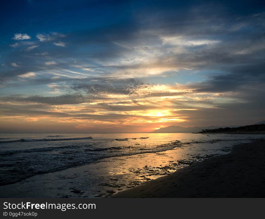 A sunset on a beach with calm seas. A sunset on a beach with calm seas.