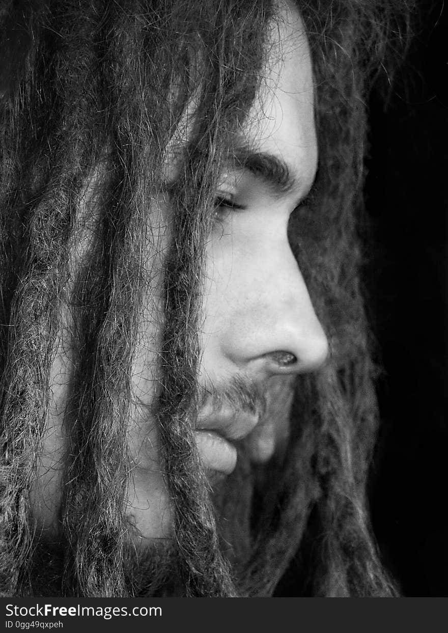 Closeup black and white profile of a serious young man with dreadlocks isolated on a dark background. Closeup black and white profile of a serious young man with dreadlocks isolated on a dark background.