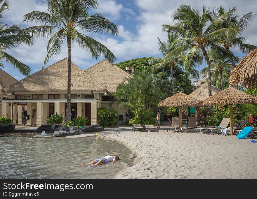 A boy lying in shallow water on a tropical beach with a holiday resort. A boy lying in shallow water on a tropical beach with a holiday resort.