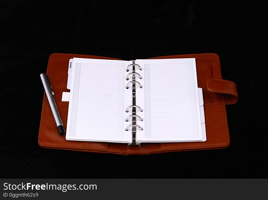 Good quality red leather notebook or diary or planner, open showing two blank pages with ring binding, and with silver pen and dark background. Good quality red leather notebook or diary or planner, open showing two blank pages with ring binding, and with silver pen and dark background.