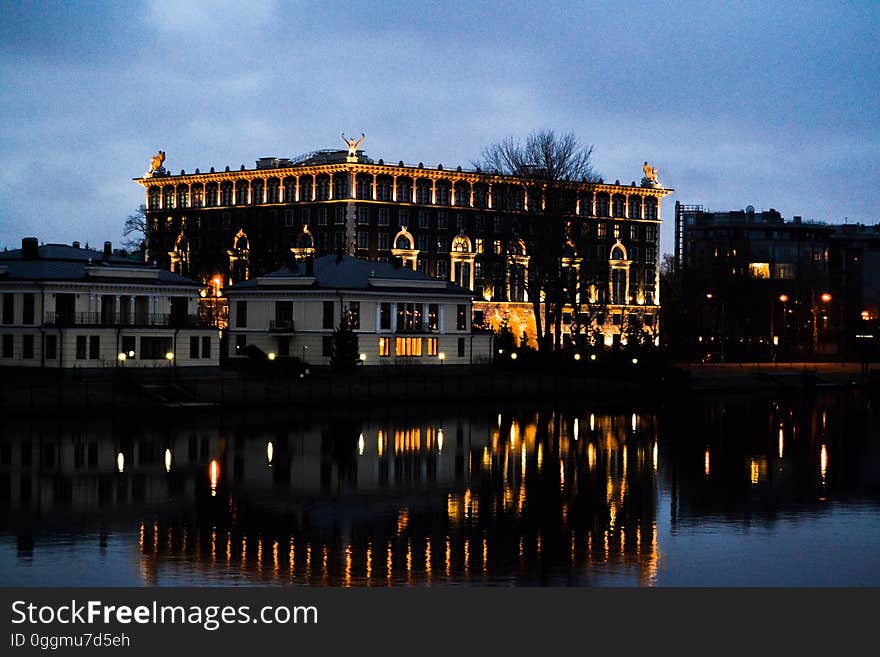 A lit hotel and houses on a river bank reflecting on the water surface. A lit hotel and houses on a river bank reflecting on the water surface.