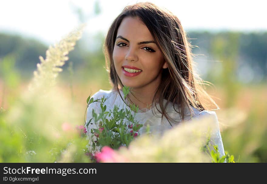 Woman in White Crew Neck Shirt Smiling and Surround With Flowers and Plants during Daytime