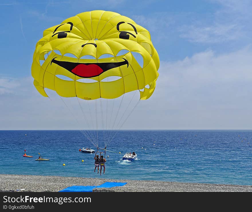 People parasailing over a beach with a yellow smiley parachute. People parasailing over a beach with a yellow smiley parachute.