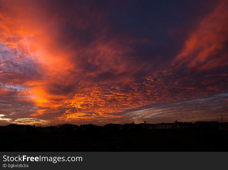 View of distant buildings in silhouette under a deep orange clouded sky. View of distant buildings in silhouette under a deep orange clouded sky.