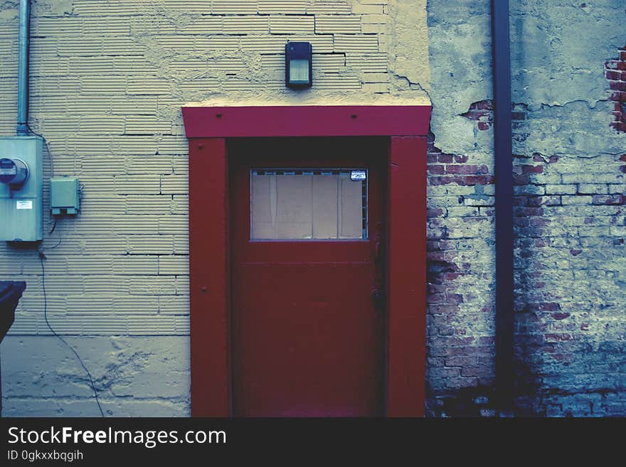 Brown door in cream painted wall with electric power point (fuse box) adjoining brick wall with cement cladding falling off.