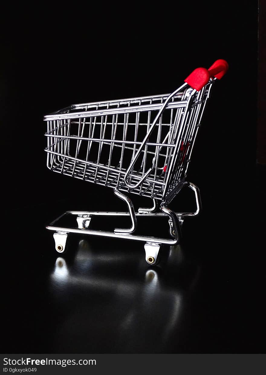 A close up of a chrome shopping cart with a red handle.