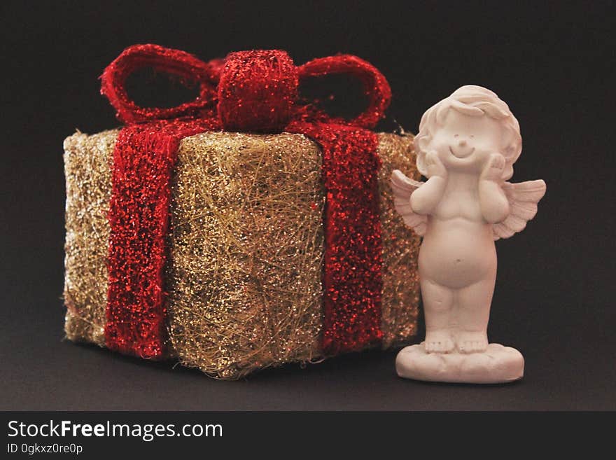 A Christmas present with a red ribbon and a miniature angel statue. A Christmas present with a red ribbon and a miniature angel statue.