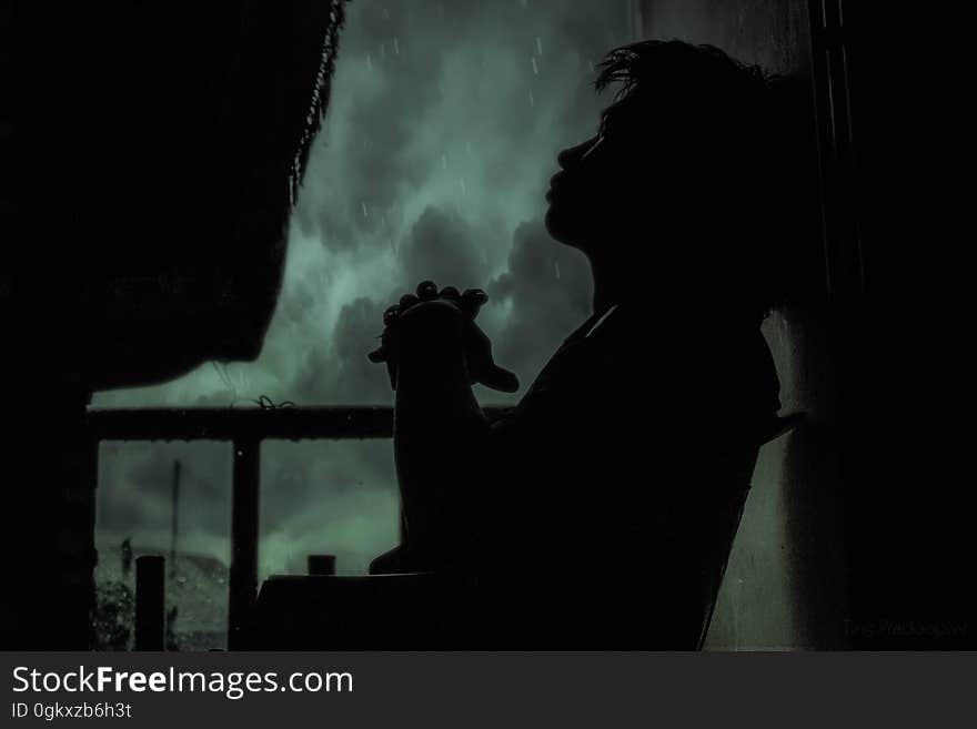 A silhouette of a pensive man sitting on a balcony in the rain at night. A silhouette of a pensive man sitting on a balcony in the rain at night.