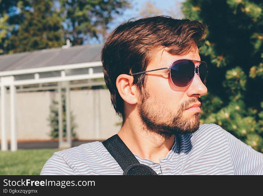 A man with sunglasses and beard sitting outdoors in the sunshine.