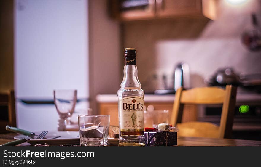 A bottle of whisky and glasses on a kitchen table.