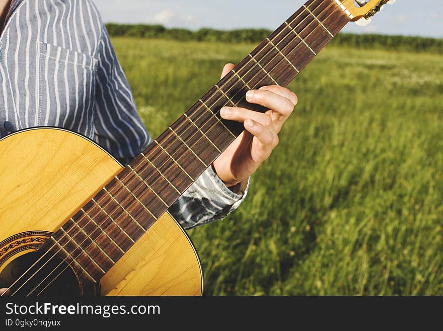 A man playing a guitar on a field in the summer. A man playing a guitar on a field in the summer.