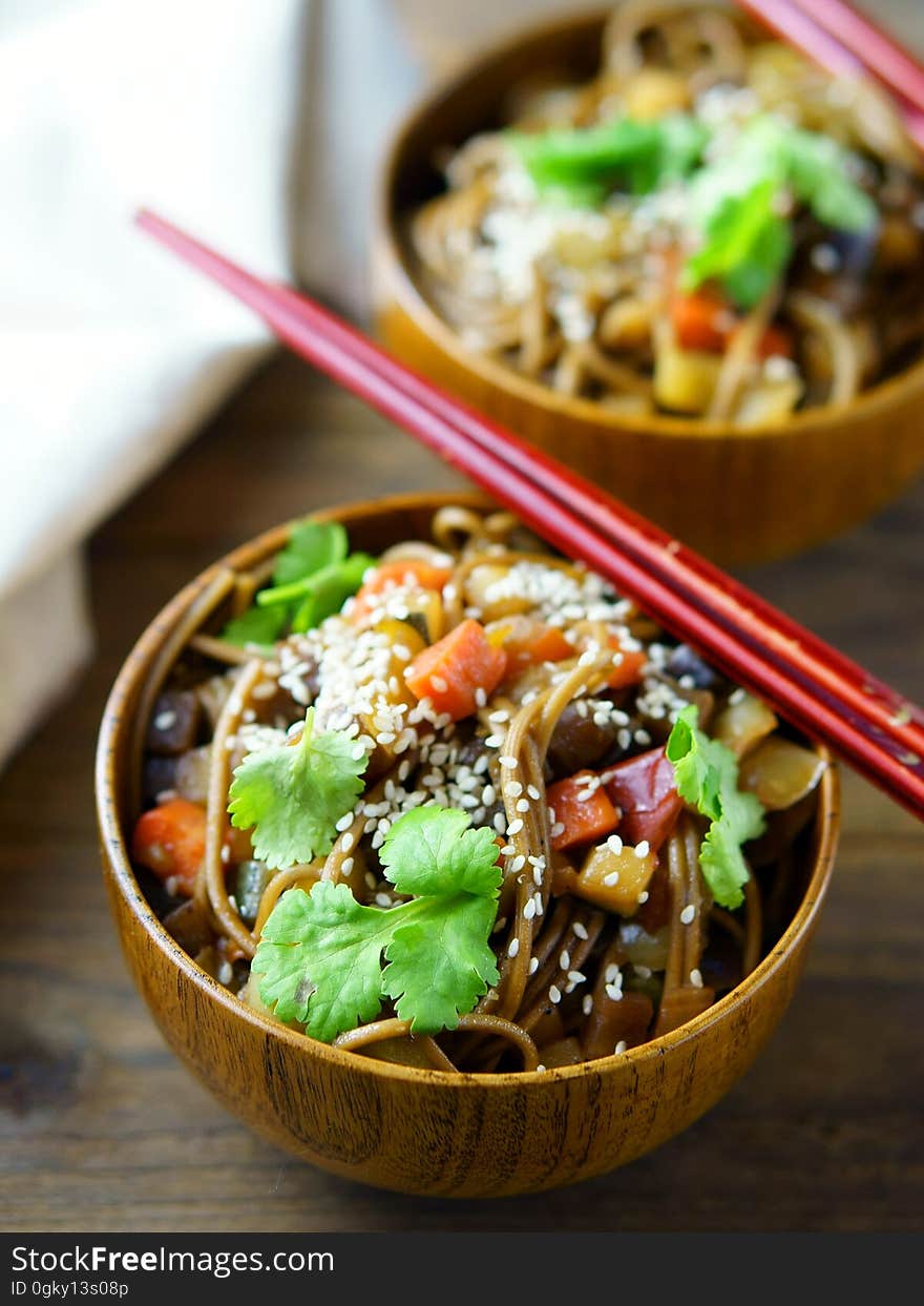 A pair of bowls with vegetables and noodles and chopsticks. A pair of bowls with vegetables and noodles and chopsticks.