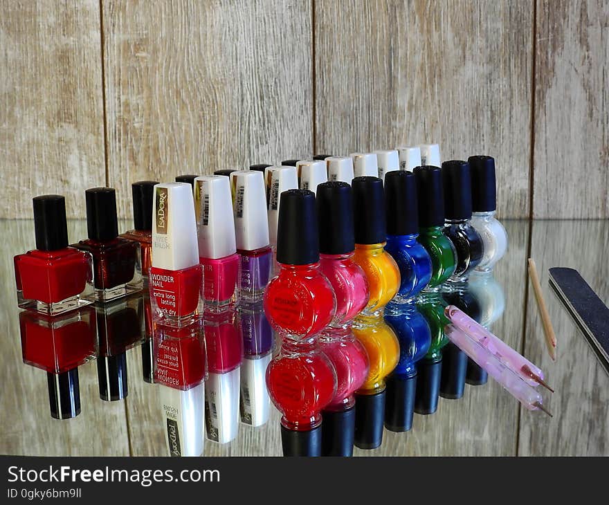 Colorful nail polish bottles with brush and file reflecting on glass background.