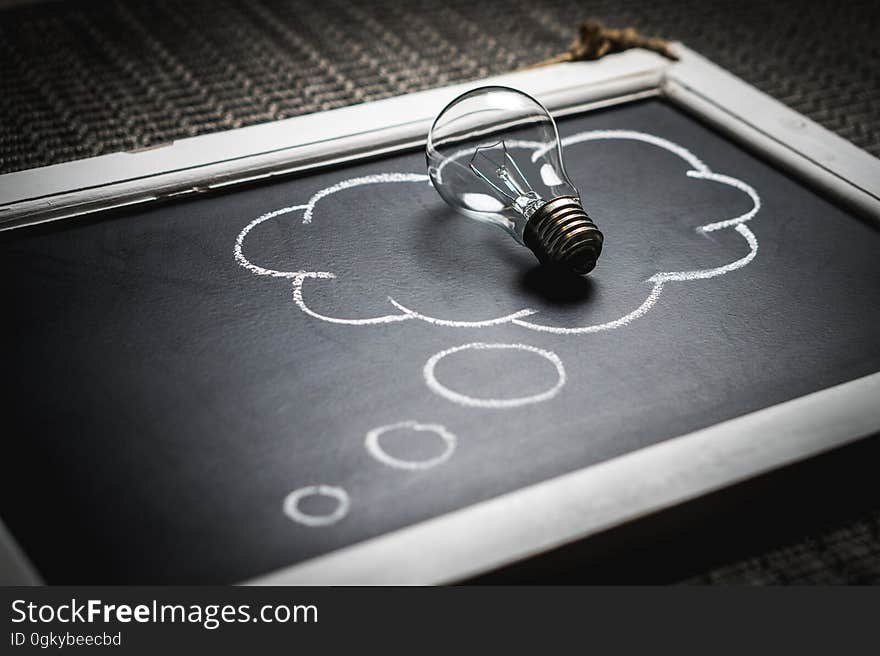 A lightbulb on a drawing of a thought bubble on a blackboard. A lightbulb on a drawing of a thought bubble on a blackboard.