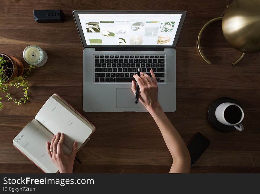 A hand typing on a laptop, a cup of coffee and a notebook on the table. A hand typing on a laptop, a cup of coffee and a notebook on the table.