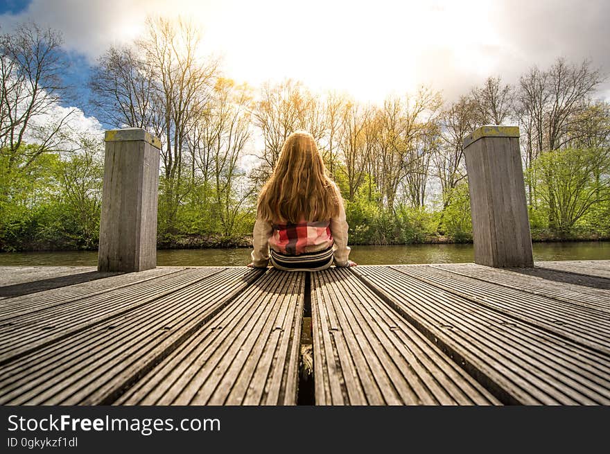 A girl sitting on a pier at lake or pond. A girl sitting on a pier at lake or pond.