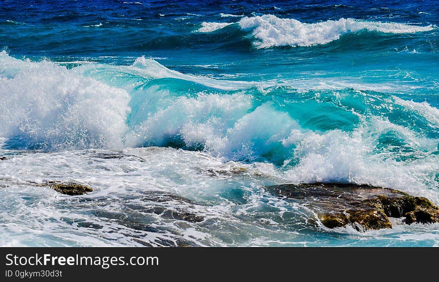 A view of the shore with blue colored waves hitting rocks. A view of the shore with blue colored waves hitting rocks.