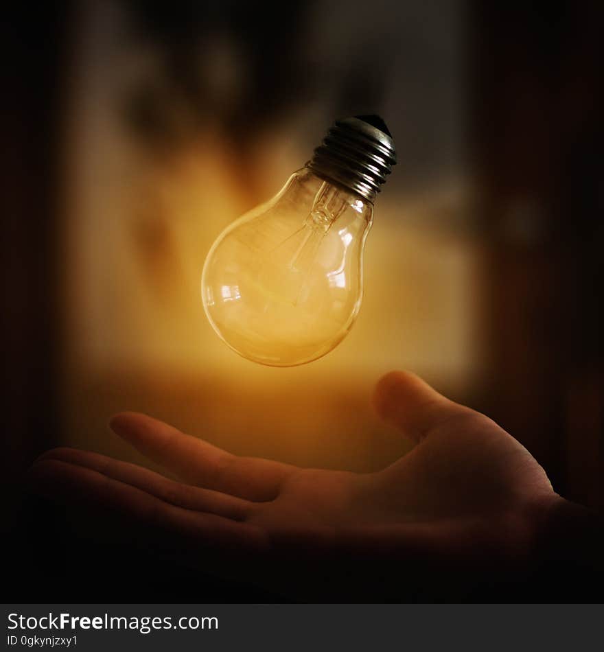 A close up of a light bulb levitating above a hand. A close up of a light bulb levitating above a hand.