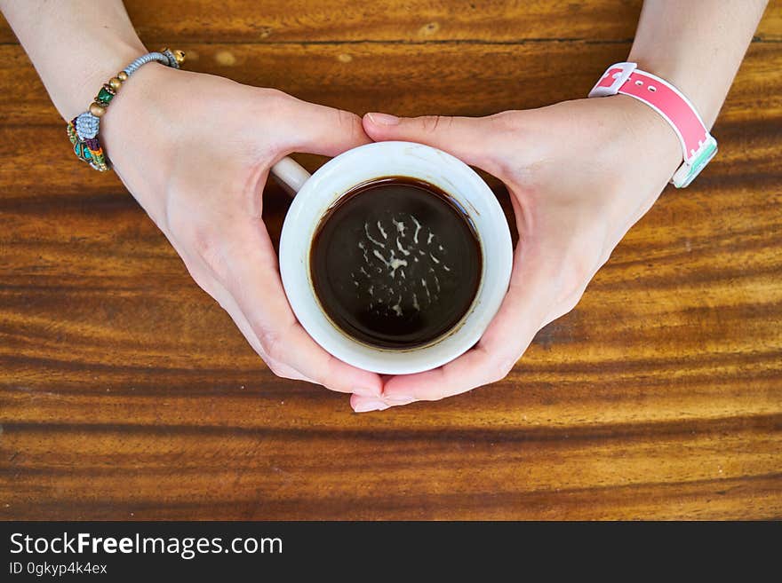 A woman holding a cup of coffee with both hands. surface. A woman holding a cup of coffee with both hands. surface